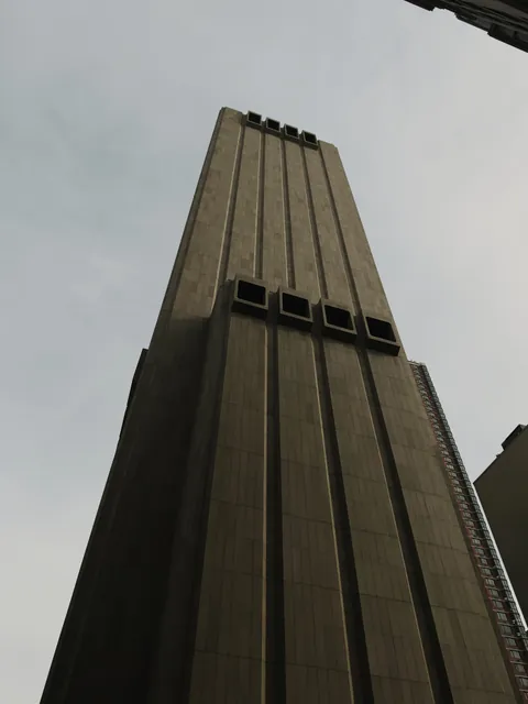 Looking up at 33 Thomas Street, a windowless brown granite tower against a pale grey sky, ribbed with vertical piers and broken only by two rows of square ventilation openings.
