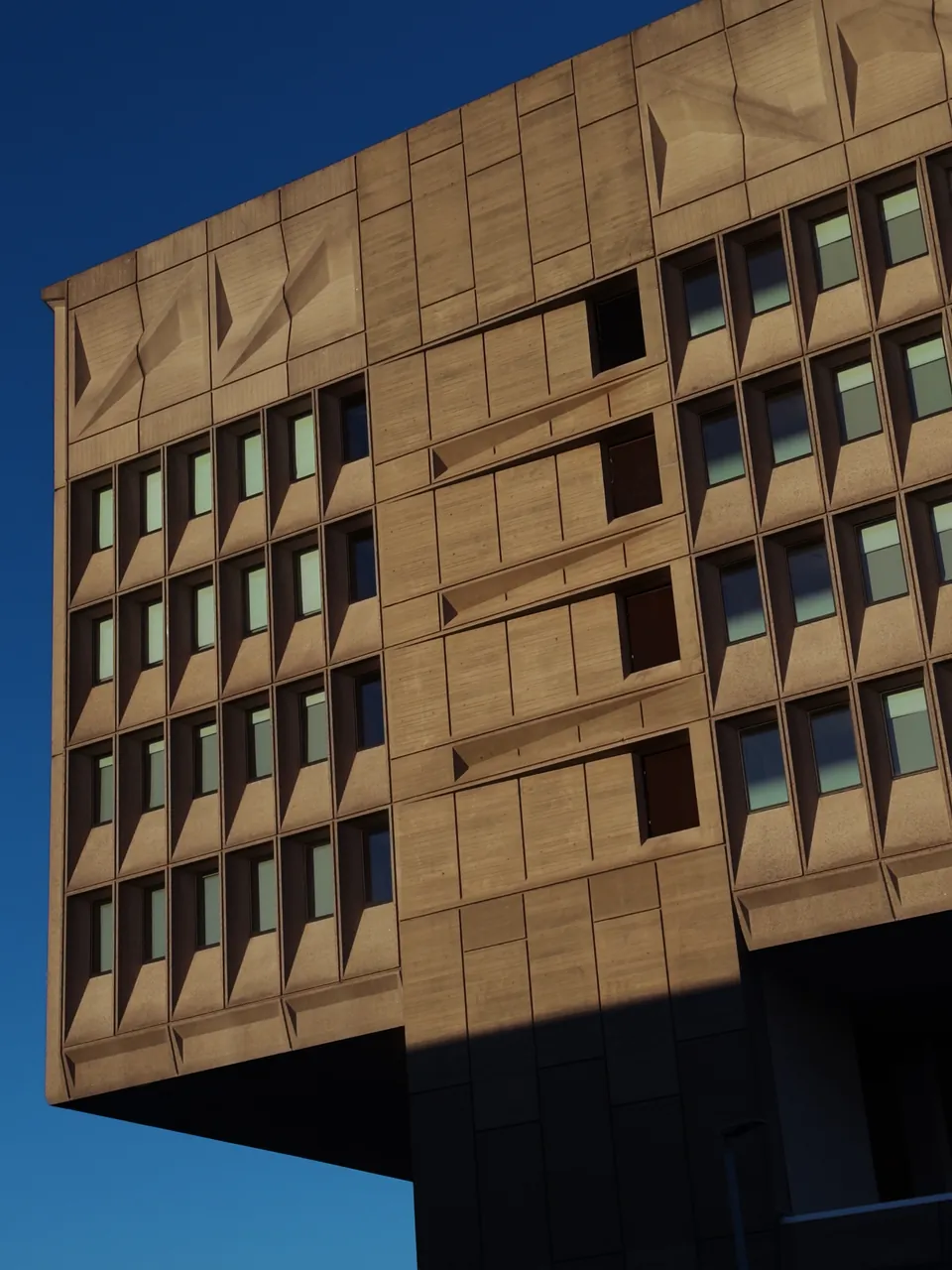 The corner of Marcel Breuer's concrete Pirelli Building against a deep blue sky, its sculpted panels and recessed windows raked by low sun.